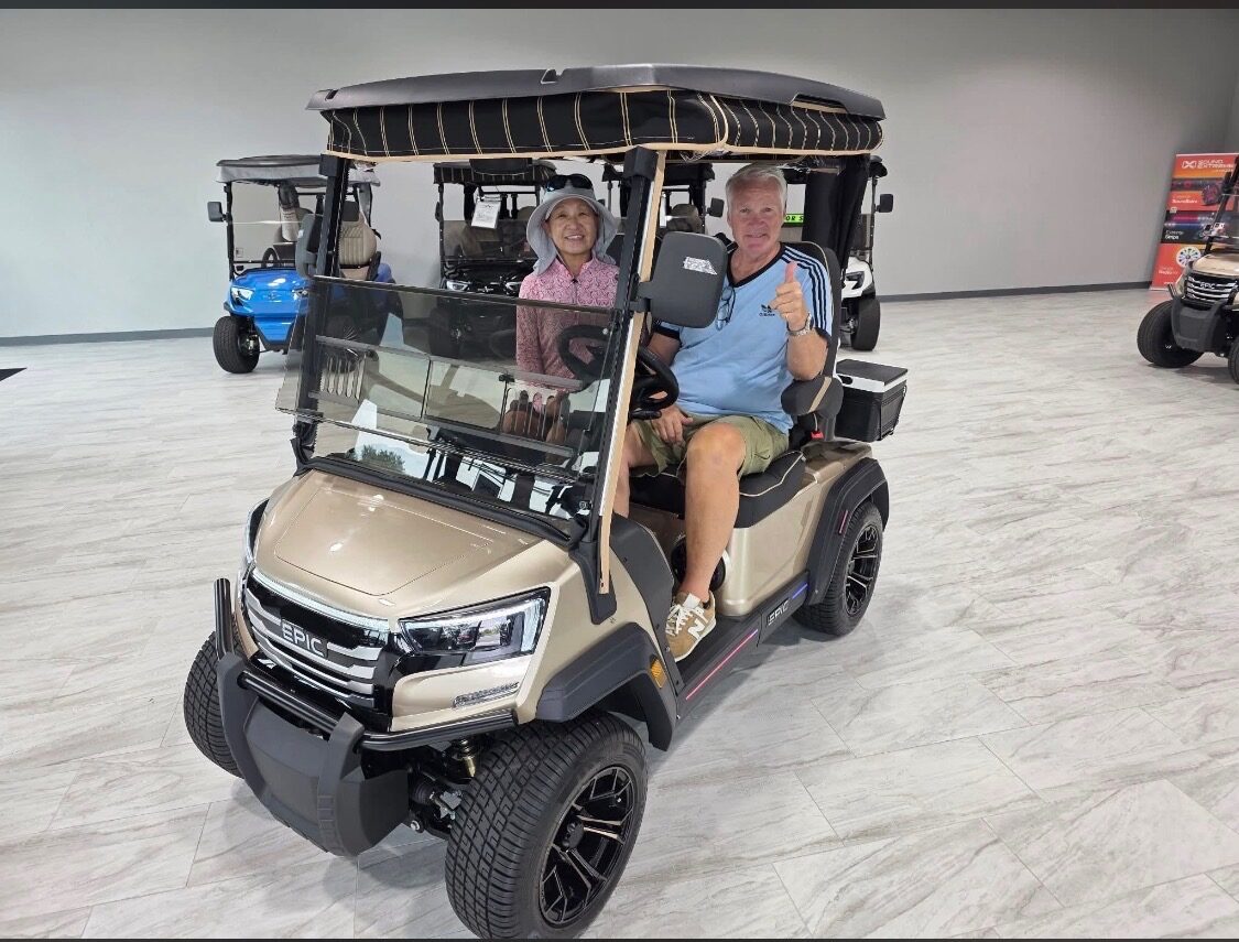 A happy customer giving a thumbs up from behind the wheel of a tan EPIC golf cart