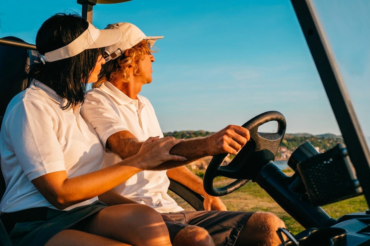 A couple cruising in an open golf cart under a bright blue sky at golden hour